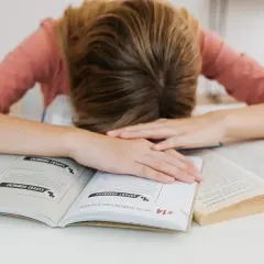 Estudiante agotado sobre libros. Aprende como controlar los nervios antes de un examen y recupera tu energía.