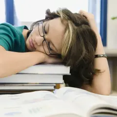 Estudiante dormida sobre libros, buscando cómo tener motivación para seguir estudiando.