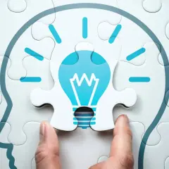 Manos ensamblan un rompecabezas que forma una cabeza con una bombilla de idea, simbolizando el aprendizaje cognitivo y la chispa de la inspiración.