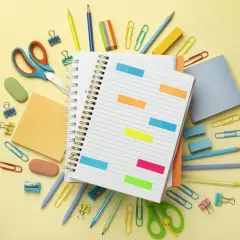 Un cuaderno abierto con notas adhesivas de colores, tijeras, lápices y clips. ¡Todo listo para como organizarme!