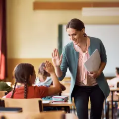 Maestra sonríe y da un cinco a una alumna, fomentando la educación personalizada en un aula con otros niños.