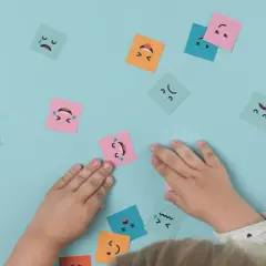 Manos de niño interactuando con tarjetas de emociones, fomentando el aprendizaje emocional.