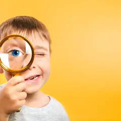 Niño con pecas mira a través de lupa dorada, ojo azul brillante. Un ejemplo de pedagogía activa, explorando el mundo con curiosidad.
