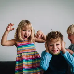 Niños expresando emociones fuertes. Una niña grita y hace gestos, otra le tapa los oídos a un niño que se ríe. Un ejemplo de la complejidad de la inteligencia emocional niños.