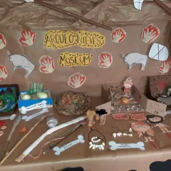 Exhibición de trabajo por proyectos infantil sobre la prehistoria: fósiles, lanzas, arcos, collares de huesos y figuras de hombres de las cavernas.
