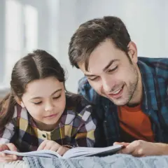 Padre e hija tumbados, ella lee en voz alta mientras él escucha atentamente.