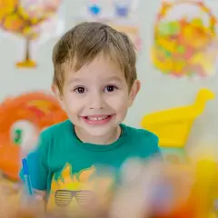 Niño sonriente con camiseta verde, rodeado de materiales educativos que fomentan la autoestima niños.