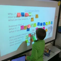 Un niño escribe en un pizarrón interactivo con preguntas para fomentar rutinas de pensamiento sobre el espacio.