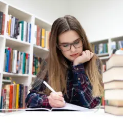 Joven concentrada en su estudio biblioteca en casa, rodeada de estanterías llenas de libros.