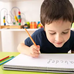 Niño concentrado practicando lectoescritura con lápiz y colores. Aprende el abecedario en su cuaderno.