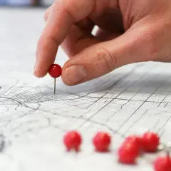 Una mano coloca un alfiler rojo sobre un mapa, marcando puntos clave para planificar rutas de aprendizaje y explorar nuevas posibilidades.