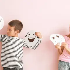 Niños exploran la **educación emocional que es** al sostener máscaras con diferentes expresiones.