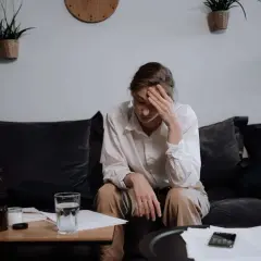 Mujer sentada en un sofá, con la mano en la frente, como si se recuperara la memoria perdida por estrés.