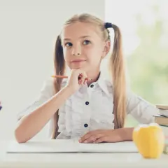 Niña pensativa con lápiz, rodeada de útiles escolares y libros. Ideas para **técnicas de estudio para niños**.