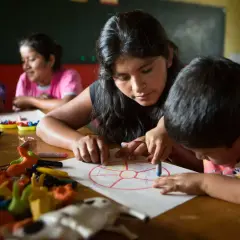 Joven guía a niños en actividad de educación en valores infantil, coloreando un círculo dividido en secciones.