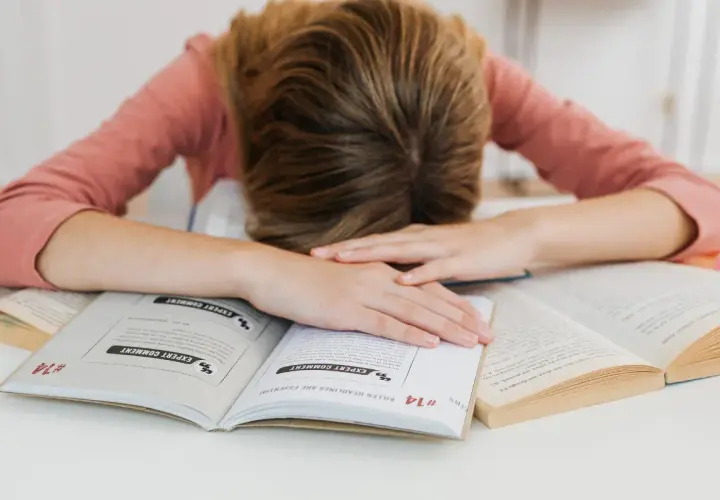 Estudiante agotado sobre libros. Aprende como controlar los nervios antes de un examen y recupera tu energía.