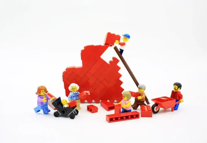 Figuras de Lego construyen un corazón rojo, simbolizando la bisquerra educación emocional y el trabajo en equipo familiar.