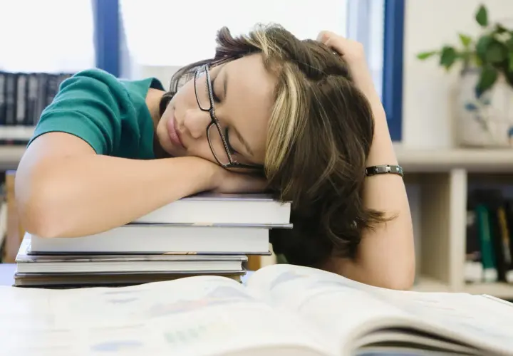 Estudiante dormida sobre libros, buscando cómo tener motivación para seguir estudiando.