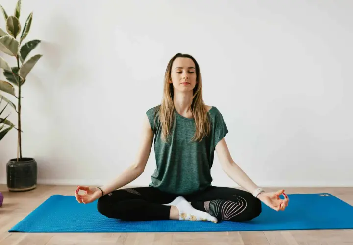 Mujer meditando en postura de loto sobre una esterilla azul. Sus ojos están cerrados, buscando calmar ansiedad y relajar la mente.