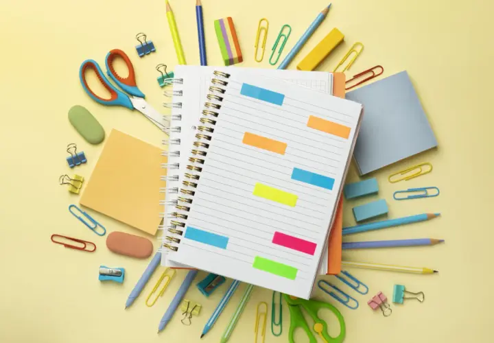 Un cuaderno abierto con notas adhesivas de colores, tijeras, lápices y clips. ¡Todo listo para como organizarme!