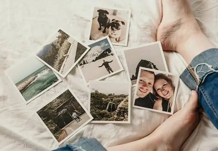 Fotos esparcidas sobre una cama blanca, evocando distorsiones de la memoria: parejas sonrientes, perros, paisajes y aventuras.