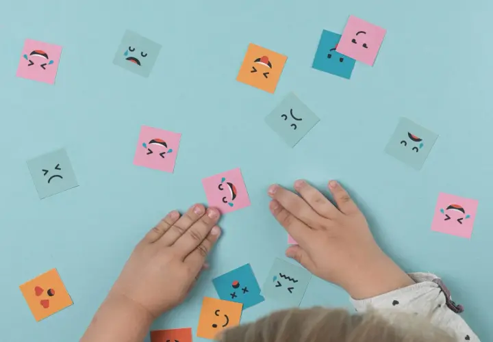 Manos de niño interactuando con tarjetas de emociones, fomentando el aprendizaje emocional.