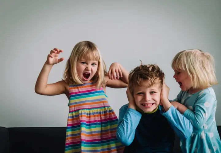 Niños expresando emociones fuertes. Una niña grita y hace gestos, otra le tapa los oídos a un niño que se ríe. Un ejemplo de la complejidad de la inteligencia emocional niños.