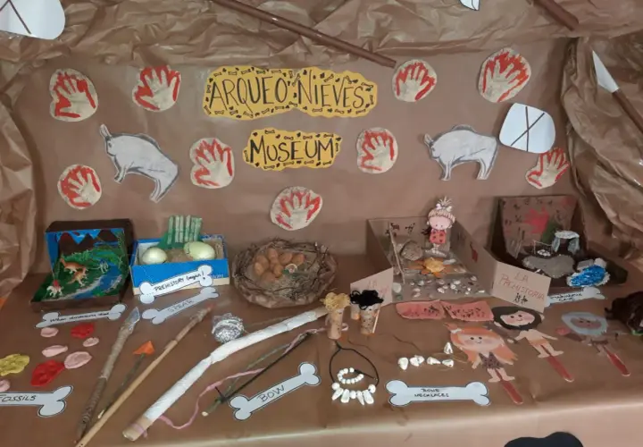 Exhibición de trabajo por proyectos infantil sobre la prehistoria: fósiles, lanzas, arcos, collares de huesos y figuras de hombres de las cavernas.