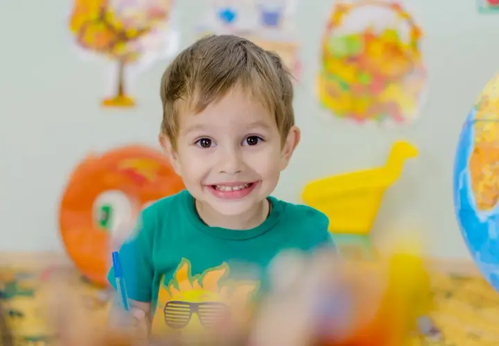 Niño sonriente con camiseta verde, rodeado de materiales educativos que fomentan la autoestima niños.