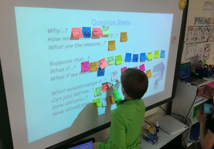 Un niño escribe en un pizarrón interactivo con preguntas para fomentar rutinas de pensamiento sobre el espacio.