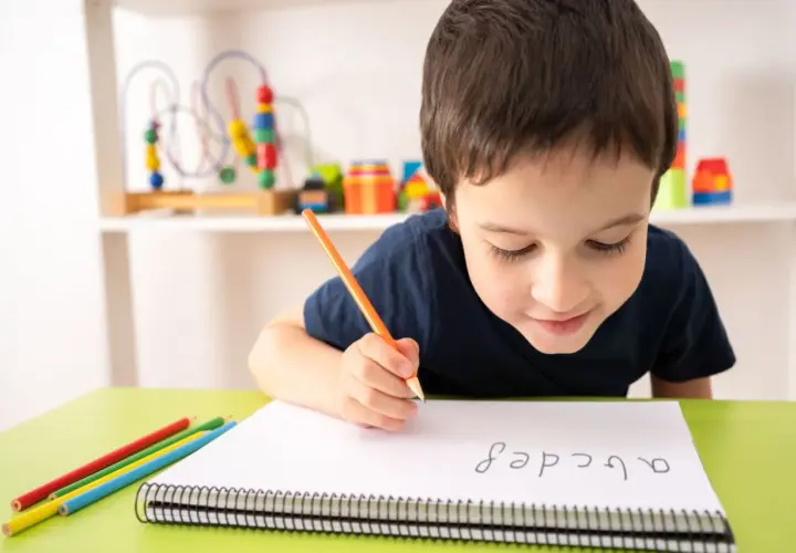 Niño concentrado practicando lectoescritura con lápiz y colores. Aprende el abecedario en su cuaderno.