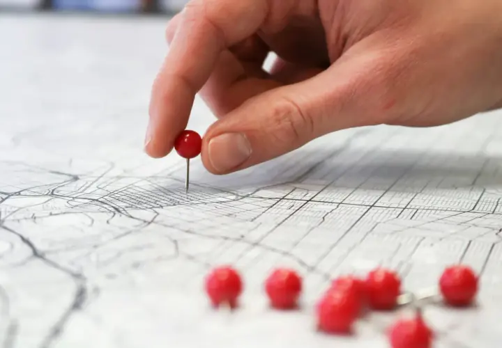 Una mano coloca un alfiler rojo sobre un mapa, marcando puntos clave para planificar rutas de aprendizaje y explorar nuevas posibilidades.