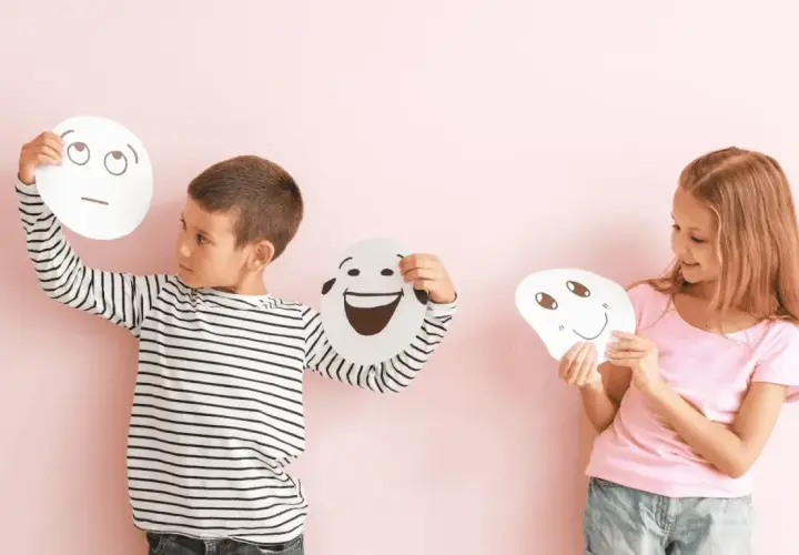 Niños exploran la **educación emocional que es** al sostener máscaras con diferentes expresiones.