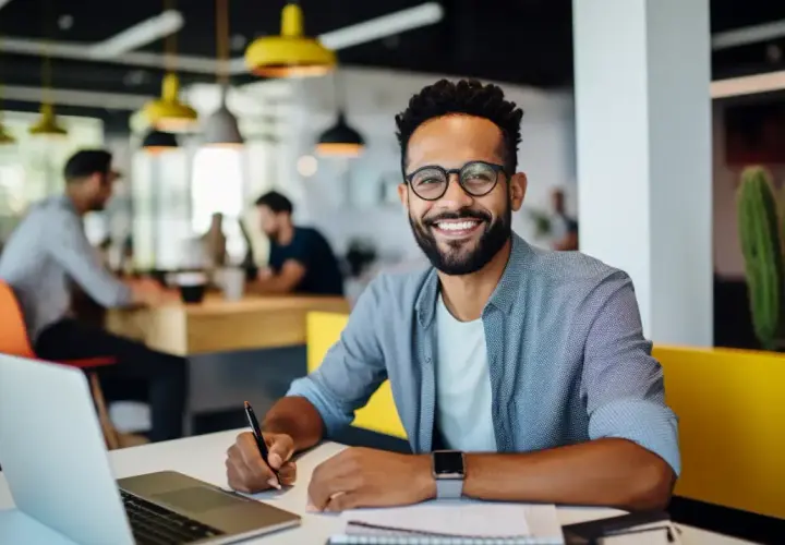 Hombre sonriente trabaja en su portátil, aplicando **técnicas de aprendizaje** en un espacio moderno.