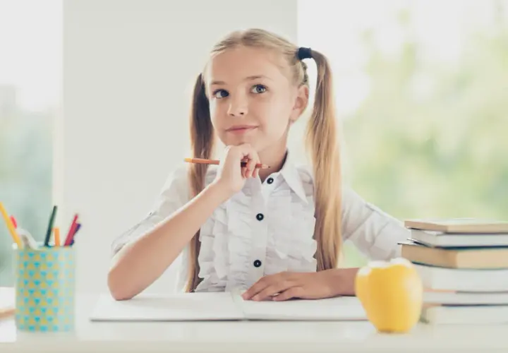 Niña pensativa con lápiz, rodeada de útiles escolares y libros. Ideas para **técnicas de estudio para niños**.