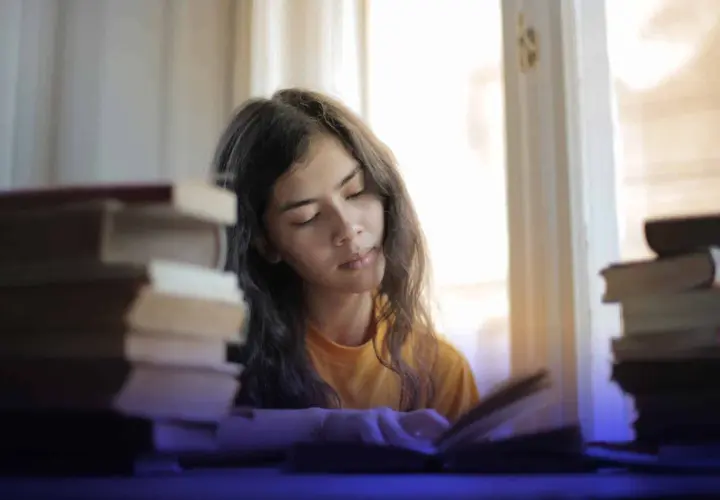 Joven concentrada estudiando, rodeada de libros, buscando técnicas para como memorizar fechas importantes.