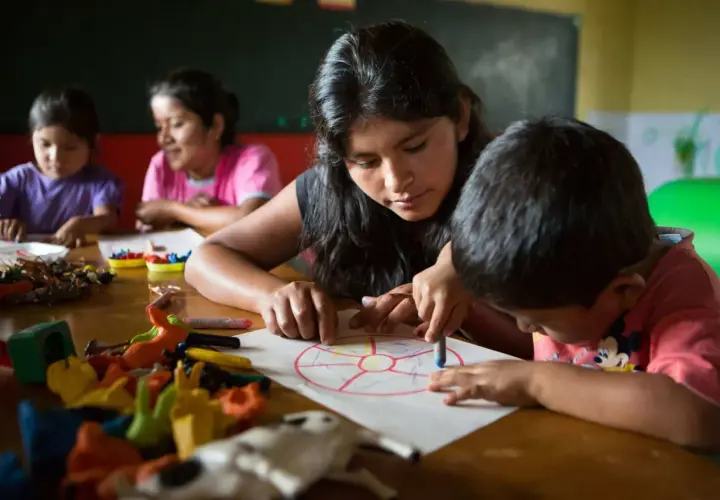 Joven guía a niños en actividad de educación en valores infantil, coloreando un círculo dividido en secciones.