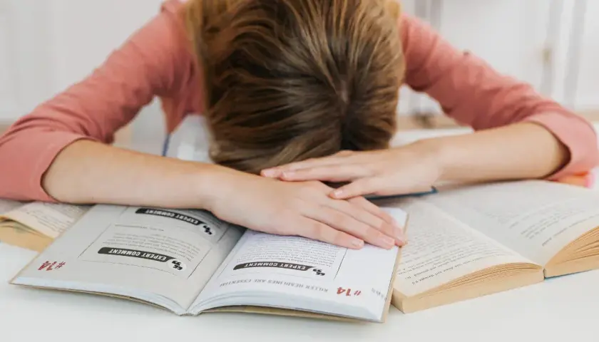 Estudiante agotado sobre libros. Aprende como controlar los nervios antes de un examen y recupera tu energía.