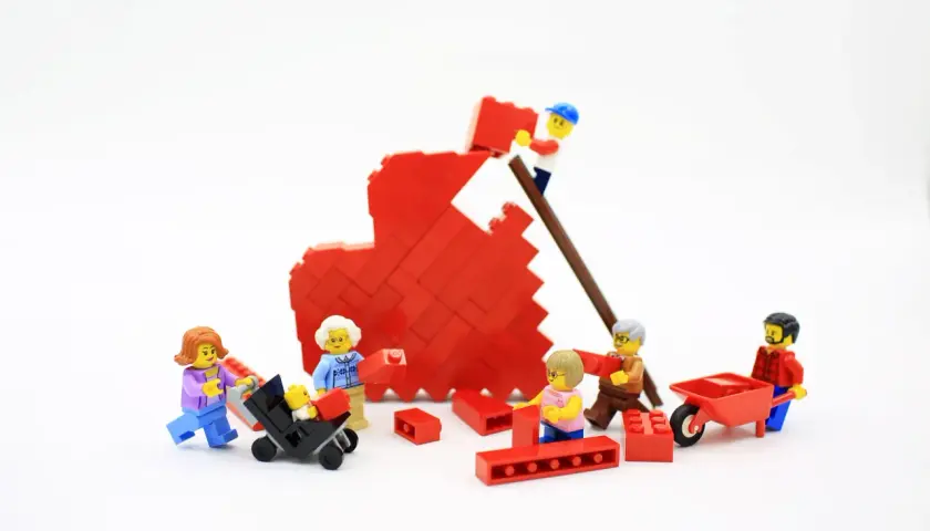 Figuras de Lego construyen un corazón rojo, simbolizando la bisquerra educación emocional y el trabajo en equipo familiar.