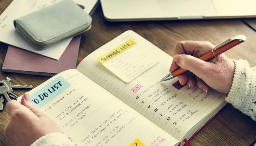 Persona escribe en un diario para aprender a escribir, con listas de tareas y comidas.
