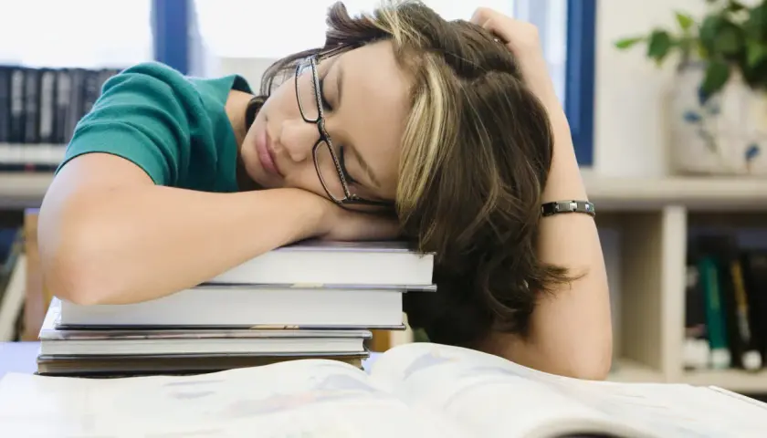 Estudiante dormida sobre libros, buscando cómo tener motivación para seguir estudiando.