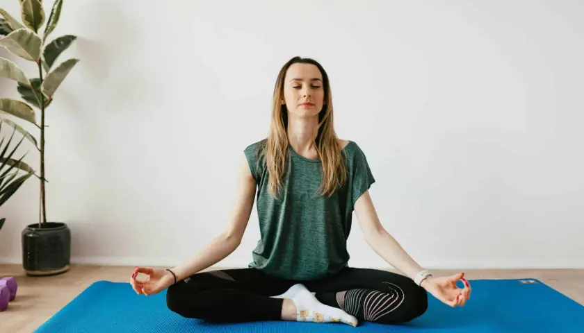 Mujer meditando en postura de loto sobre una esterilla azul. Sus ojos están cerrados, buscando calmar ansiedad y relajar la mente.