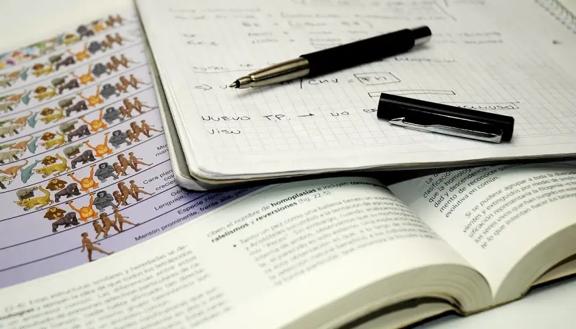 Apuntes para estudiar: cuaderno con notas, bolígrafo, libro abierto y lámina de evolución.