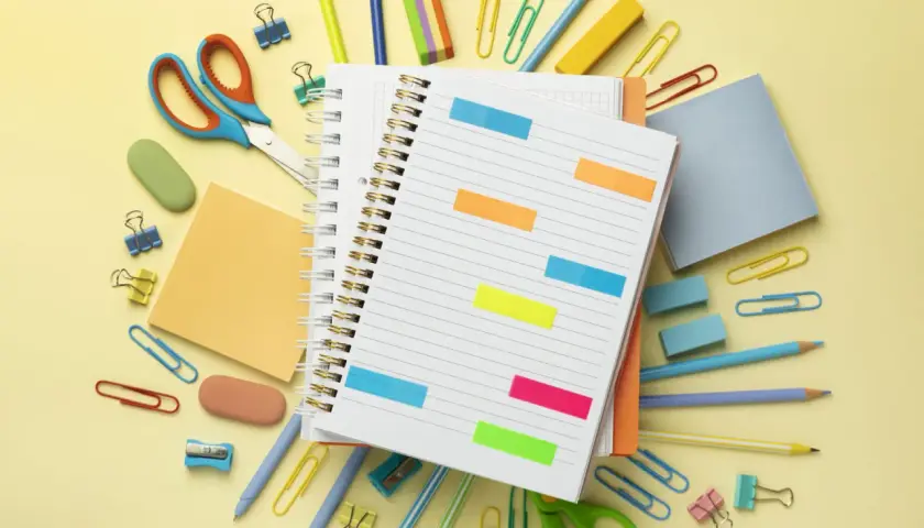 Un cuaderno abierto con notas adhesivas de colores, tijeras, lápices y clips. ¡Todo listo para como organizarme!
