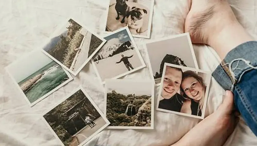 Fotos esparcidas sobre una cama blanca, evocando distorsiones de la memoria: parejas sonrientes, perros, paisajes y aventuras.