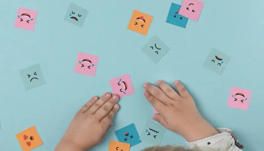 Manos de niño interactuando con tarjetas de emociones, fomentando el aprendizaje emocional.