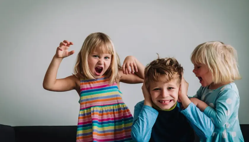 Niños expresando emociones fuertes. Una niña grita y hace gestos, otra le tapa los oídos a un niño que se ríe. Un ejemplo de la complejidad de la inteligencia emocional niños.