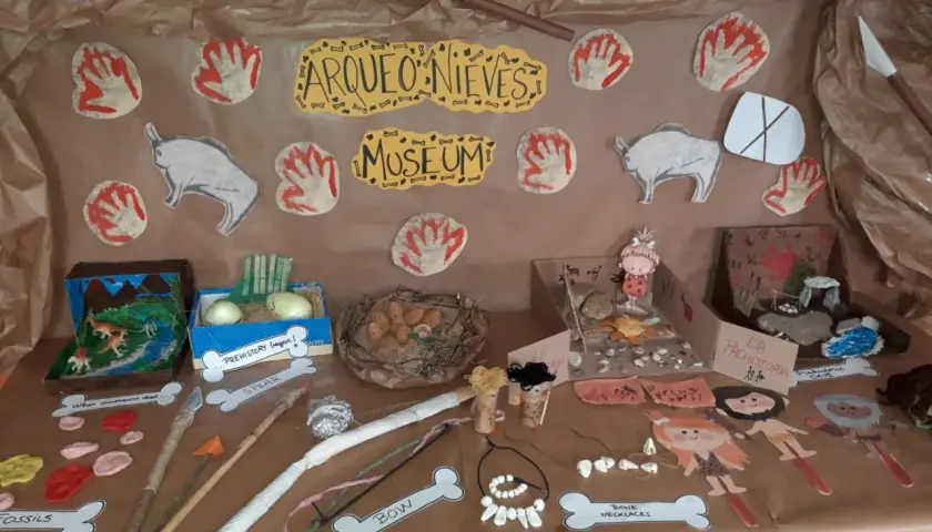 Exhibición de trabajo por proyectos infantil sobre la prehistoria: fósiles, lanzas, arcos, collares de huesos y figuras de hombres de las cavernas.