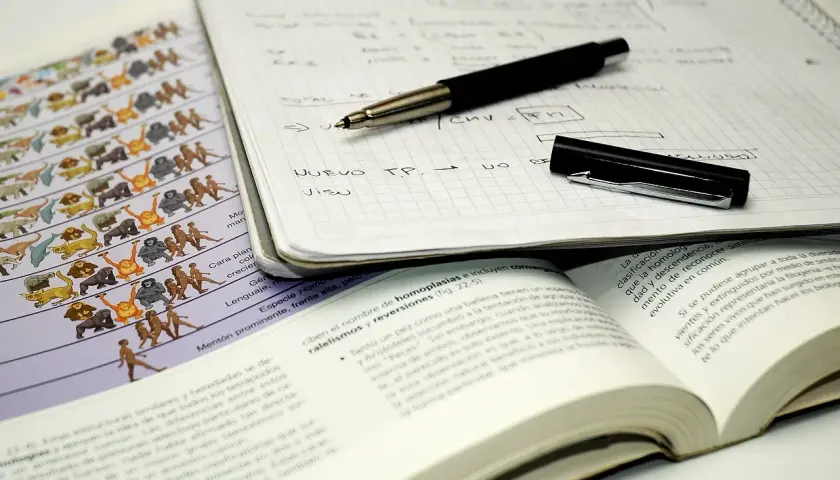 Cuaderno con notas, bolígrafo y libro abierto. El método Cornell se aplica en el estudio de la evolución, como muestra la imagen.