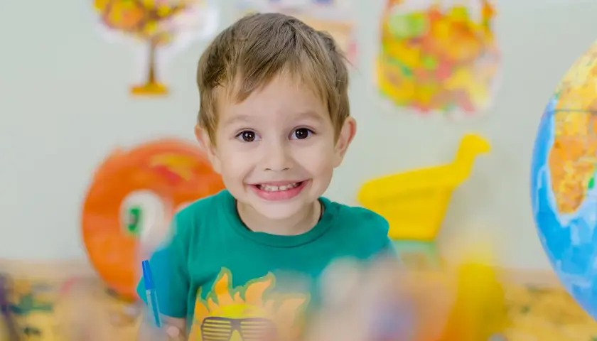 Niño sonriente con camiseta verde, rodeado de materiales educativos que fomentan la autoestima niños.
